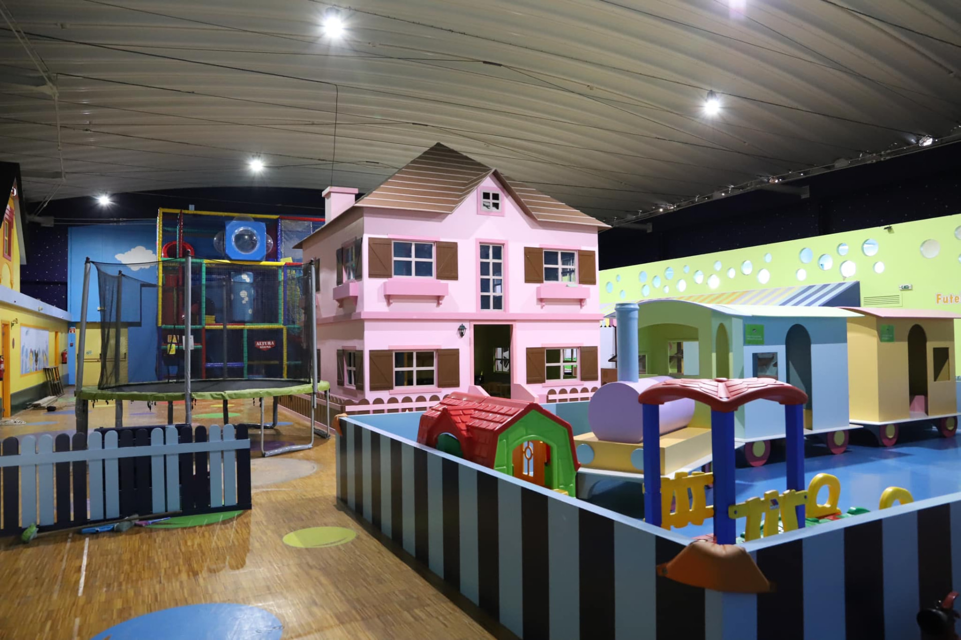Zona de brincadeira do Ateliê de Festas com casa de bonecas, trampolim e comboio